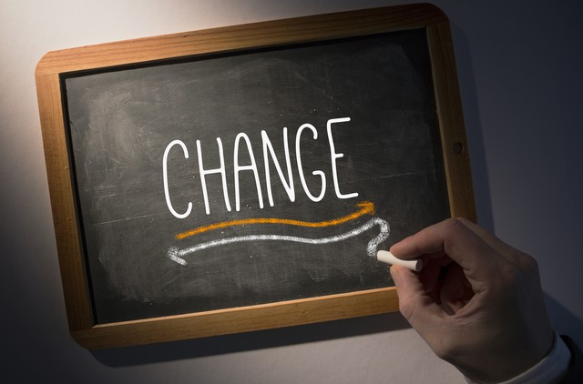 Hand writing the word change on black chalkboard